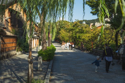 Anonymous people strolling in old city district near wooden houses and green trees