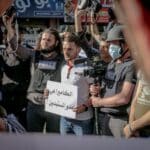 Group of ethnic journalists with placard with Arabic inscription and cameras at demonstration against policy