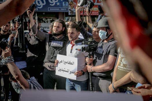 Group of ethnic journalists with placard with Arabic inscription and cameras at demonstration against policy