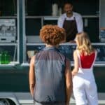 Back view of diverse clients standing near street food truck and choosing lunch