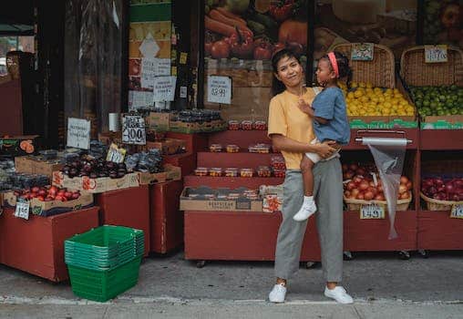 Content Asian mother holding daughter on hands near market stall