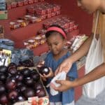 Ethnic girl choosing fruit in market with mother