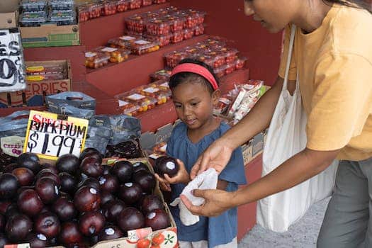 Ethnic girl choosing fruit in market with mother