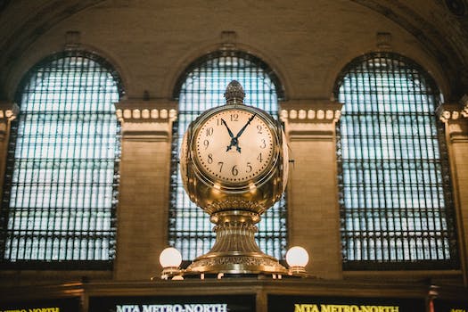 From below of aged retro golden clock placed atop information booth of historic Grand Central Terminal with arched windows