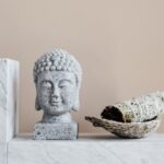 Stone Buddha and sage incense bundle in bowl on marble shelf
