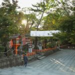 Unrecognizable people walking on paved pathway near green trees while sightseeing ancient Yasaka Shrine located in Kyoto
