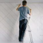 Faceless house painter undercoating wall in bright room