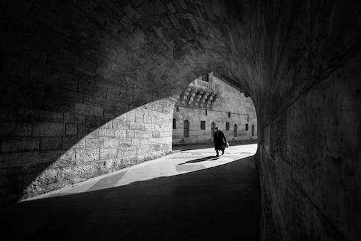 Black and white anonymous male walking along old stone tunnel near aged brick building