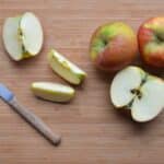 Slices of ripe apples and knife on wooden surface
