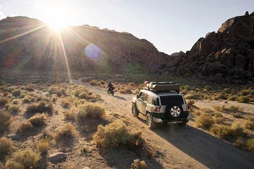 Breathtaking landscape with rocky hills and dry vegetation against sundown and car with motorbike on narrow dusty road