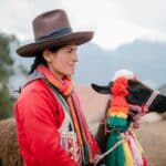 Concentrated Peruvian woman standing in village with adorable lama with multicolored tassels on head