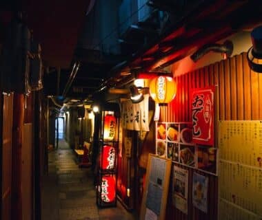Narrow street with traditional Japanese izakaya bars decorated with hieroglyphs and traditional red lanterns in evening