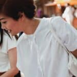 Positive Asian women in white blouses spending sunny day in street market and choosing goods
