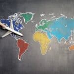Top view of crop anonymous person holding toy airplane on colorful world map drawn on chalkboard
