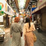 Back view of unrecognizable trendy female travelers in stylish clothes walking in traditional famous Nishiki Market in Kyoto