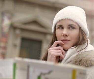 Concentrated female in warm hat and coat looking for right way while standing with map in street