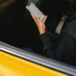 Crop passenger with navigator app on smartphone in taxi vehicle