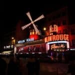 Exterior of famous cabaret club with glowing neon light illumination and banners decorate with luminous mill and located on street of Paris at night