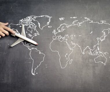 From above of crop anonymous person driving toy airplane on empty world map drawn on blackboard representing travel concept