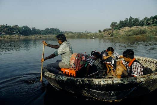 Group of Indian man and schoolchildren with backpacks sitting in handmade boat while floating on water to school