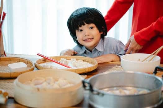 Positive ethnic boy sitting at table with homemade Chinese dumplings on bamboo plates for steamer